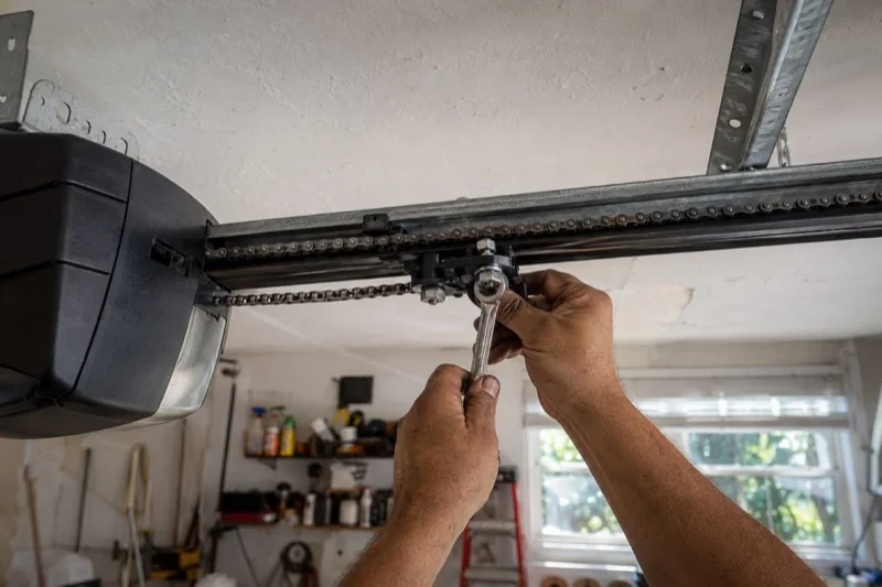 Hands holding a wrench against an opener trolley beneath a chain rail