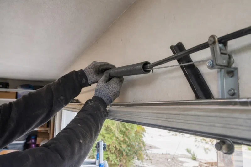 Gloved hands holding a long spring beside an overhead garage-door track